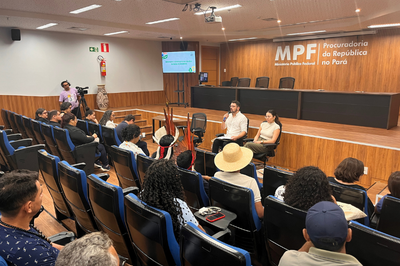 Auditório com público sentado, pessoas em uma mesa, e ao fundo, uma parede de madeira com o logo "MPF Procuradoria da República no Pará".