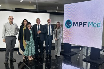 Foto mostra seis pessoas em pé ao lado de banner do MPFMed