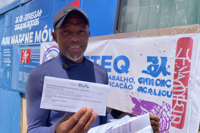 Um homem negro de pele retinta sorrindo para a foto. Em sua mão, tem um documento.