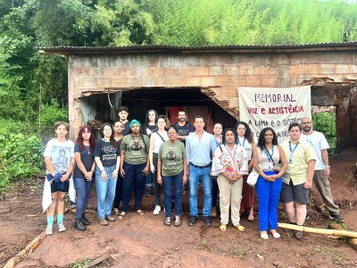 Grupo de pessoas posa em pé, na frente de casa atingida pela lama na comunidade de Gesteira Velho