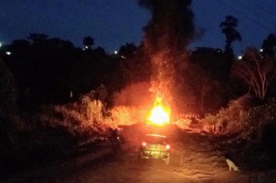 Ponte foi queimada para obstruir a passagem de fiscais. Foto: Inquérito policial Foto noturna mostra carro em estrada de terra escura, com uma grande e intensa coluna de fogo no centro da cena.