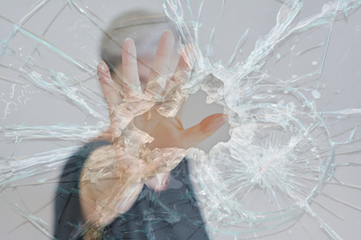 Mulher com a mão estendida em uma atitude defensiva atrás de um vidro quebrado