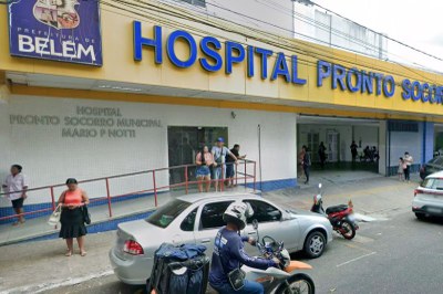 Fachada amarela com letreiro azul "Hospital Pronto-Socorro" e logo da Prefeitura de Belém. Pessoas estão na rampa e veículos transitam na rua à frente.