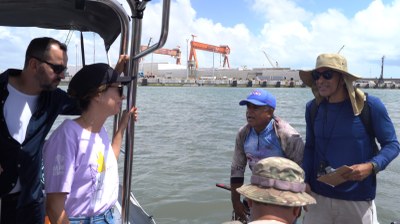 Foto: Diego Fernandes (IP) a procuradora da República, dentro do barca da PF, fala com pescadores que estão em outro barco; ao fundo, aparecem guindastes do Porto de Suape