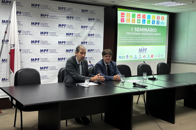 A imagem mostra um ambiente de conferência ou seminário, possivelmente no Ministério Público Federal (MPF) em Minas Gerais, como indicado pelos logotipos e textos no fundo. Dois homens estão sentados em uma mesa preta na frente de uma tela de projeção. O homem à esquerda tem barba e veste um terno escuro e gravata clara, enquanto o homem à direita veste um terno azul-marinho e gravata escura. A mesa tem microfones e papéis na frente deles. Na tela de projeção, em destaque, está escrito "I SEMINÁRIO Programa Participa Minas" e, abaixo, uma descrição sobre "Fomento a projetos intersetoriais de extensão universitária em interface com a pesquisa visando ao desenvolvimento sustentável e prevenção, mitigação e correção dos impactos da mineração no Estado de Minas Gerais". No topo da tela, são visíveis os ícones dos Objetivos de Desenvolvimento Sustentável (ODS) da ONU.