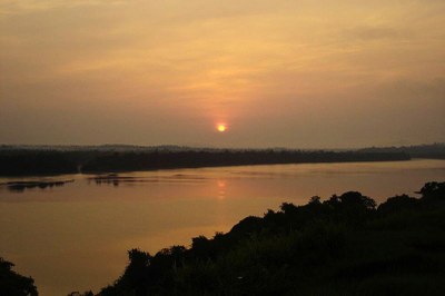 Parna Serra do Pardo. Foto: Ricardo Dagnino, sob licença CC BY-SA 3.0. Fotografia de um pôr do sol alaranjado sobre o Rio Xingu, largo e calmo, com a margem coberta por uma densa faixa de mata, do Parque Nacional da Serra do Pardo.