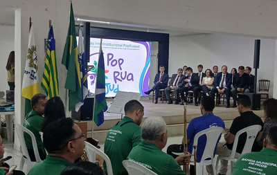 Foto: DIvulgação Imagem do evento institucional PopRuaJud em Picos (PI, ocorrido no dia 28 de novembro de 2025. No ambiente, há várias pessoas sentadas nas cadeiras brancas, de costas para a câmera, ou parcialmente visíveis. Muitos deles estão vestindo camisas ou camisetas verdes que parecem ser uniformes. No fundo, sobre um palco, há um grupo de autoridades ou convidados sentados em cadeiras estofadas escuras. Todos estão vestindo trajes sociais, como ternos. Há cerca de dez pessoas visíveis nesta área.