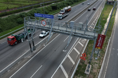 Free Flow na Via Dutra. Foto: Divulgação Motiva Rodovias Imagem de trecho da Via Dutra onde se vê o pórtico de cobrança do Free Flow. Carros e caminhões estão circulando pelas pistas.