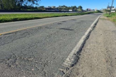  Uma estrada de asfalto com diversas rachaduras, buracos e remendos