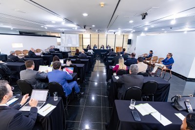 mpfebc.jpg A foto registra o seminário sobre energia e minerais estratégicos em um auditório moderno. À direita, uma mesa de honra composta por cinco autoridades está posicionada sobre um tablado; à esquerda, o público ocupa mesas organizadas em fileiras. O evento possui formato híbrido, evidenciado por uma tela de projeção ao fundo que exibe um palestrante remoto.