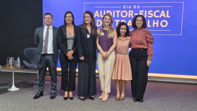 Imagem mostra pessoas em pé em frente a painel de auditório. 