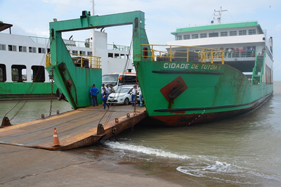 Foto de ferryboat verde e branco "Cidade de Tutóia I" com a rampa baixada, contendo veículos e pessoas em seu interior em uma área de embarque.