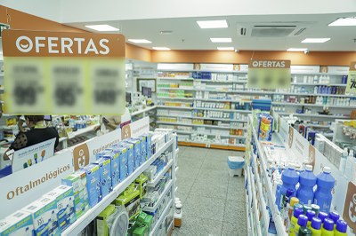 Foto de interior de uma farmácia. É possível ver clientes de costas e uma prateleiras com remédios dispostos.