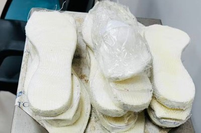 Foto: Polícia Federal Foto mostra diversas palmilhas brancas e grossas empilhadas sobre uma superfície metálica, com um pacote plástico contendo cocaína acima delas.