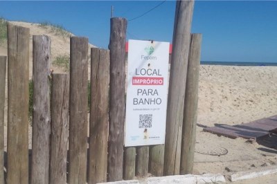 Foto mostra cerca de madeira com placa sinalizando ponto impróprio para banho em praia do Rio Grande do Sul