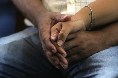 Foto: Tânia Rêgo/Agência Brasil Fotografia em close de duas mãos entrelaçadas em um gesto de apoio e união. Uma das mãos possui tatuagens discretas no pulso e no dorso, repousando sobre as mãos de outra pessoa.