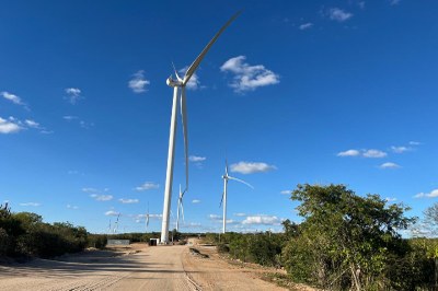 Diversas turbinas de vento brancas, altas e com três pás cada, estão alinhadas ao longo de uma estrada de terra.