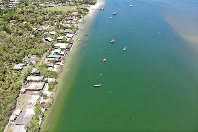 Vista aérea da face norte da Ilha das Peças (PR), onde estão localizadas as casas embargadas. Foto: Ibama/PR Imagem aérea da Ilha das Peças, no litoral do Paraná, mostrando área costeira com casas próximas à margem e vegetação nativa ao redor.
O mar aparece em tom esverdeado, com embarcações ancoradas próximas à orla.
Observa-se a ocupação humana ao longo da faixa costeira, em contraste com áreas preservadas.
A imagem evidencia a proximidade das construções com o ambiente natural e a linha da maré.