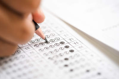 Foto: Canva. Foto mostra detalhe de uma mão com um lápis sobre folha de prova objetiva de concurso; algumas alternativas da folha estão marcadas