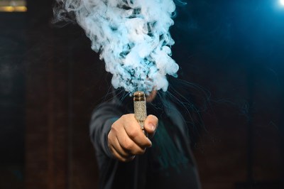 Foto: Freepik Foto mostra uma pessoa com um vape na mão. A fumaça encobre o rosto