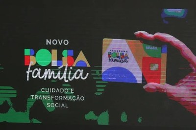 A imagem apresenta a identidade visual do novo Bolsa Família. Do lado esquerdo, sobre um fundo preto, lê-se "NOVO BOLSA família", seguida pelo slogan "CUIDADO E TRANSFORMAÇÃO SOCIAL". À direita, uma mão segura o novo modelo do cartão. 