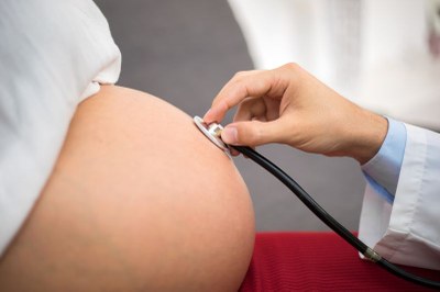 Foto em detalhe de um médico com estetoscópio examinando a barriga de uma gestante