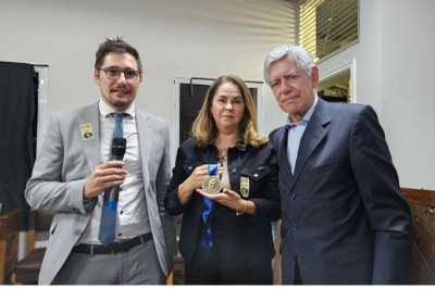 Foto: Carlito Santos Foto mostra a procuradora Eugenia Augusta Gonzaga, uma mulher branca de roupa escura, com a medalha Manoel Fiel Filho nas mãos, no centro da foto, ao lado de dois homens de terno, um mais novo de óculos e terno cinza, e outro mais velho, de cabelos brancos e terno escuro.