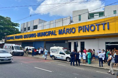  Fachada do Hospital PSM Mário Pinotti em Belém, com letreiro azul em fundo amarelo, ambulâncias estacionadas e pessoas na calçada.
