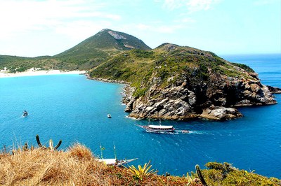Vista panorâmica de Arraial do Cabo com águas azul-turquesa, barcos navegando e morros com vegetação ao fundo